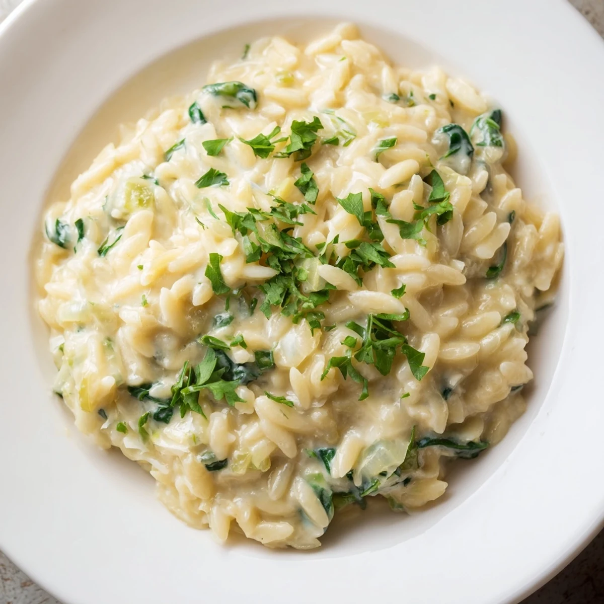 Close up of creamy, golden one-pot orzo with spinach, illustrating the richness and texture of the dish.