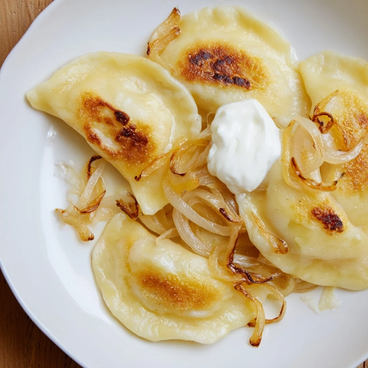 Golden-brown Polish pierogi dumplings are filled with potato and cheese, served with sweet onions.