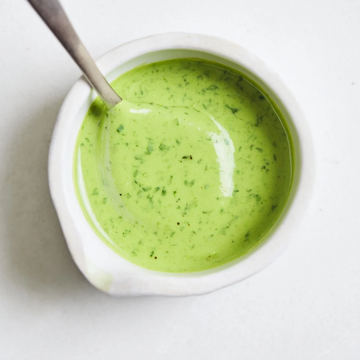 Bright Green Goddess Dressing in a glass jar beside crisp vegetables and toasted bread.