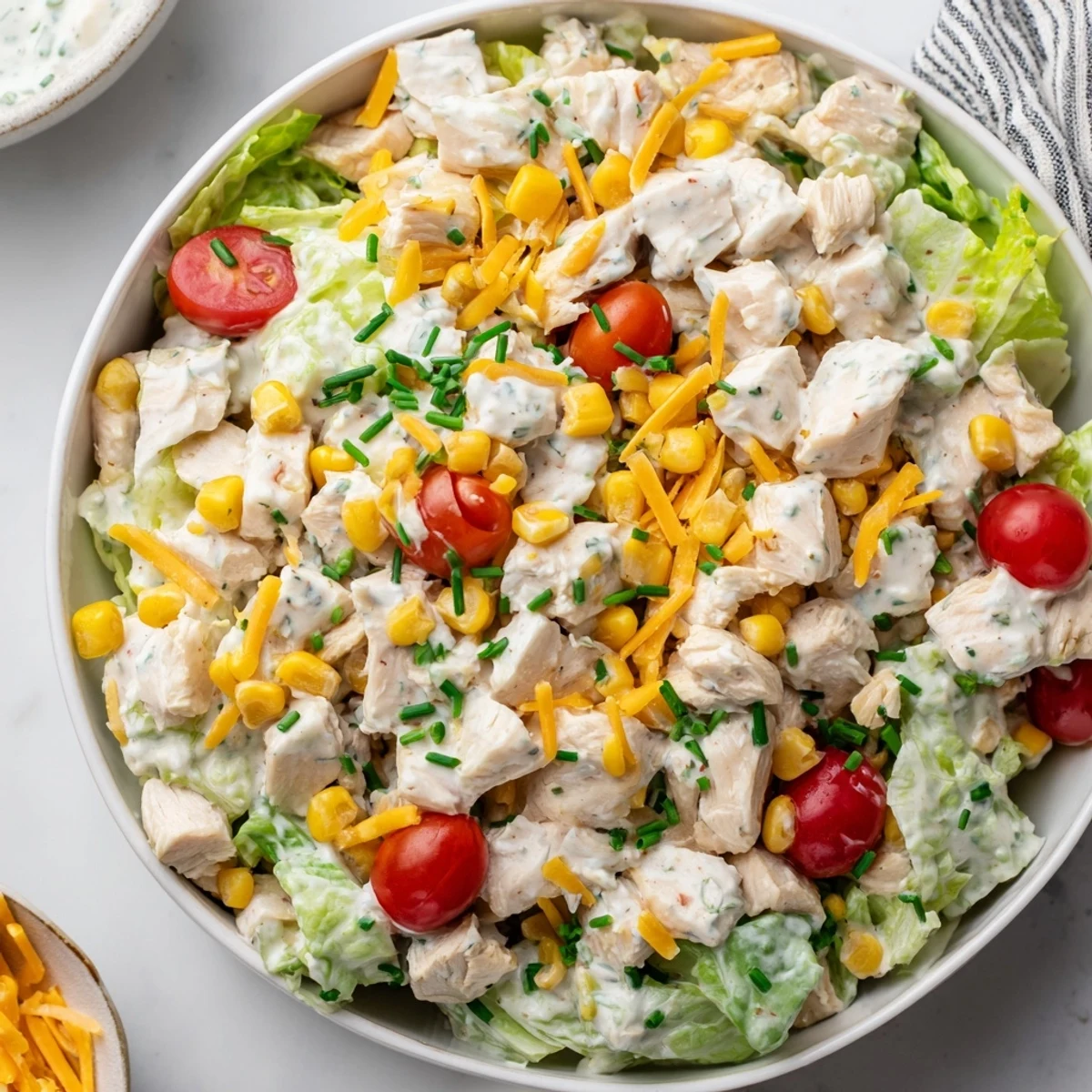 A close-up of Ranch Chicken Chopped Salad in a white bowl, featuring tender chicken, cherry tomatoes, and fresh herbs. 