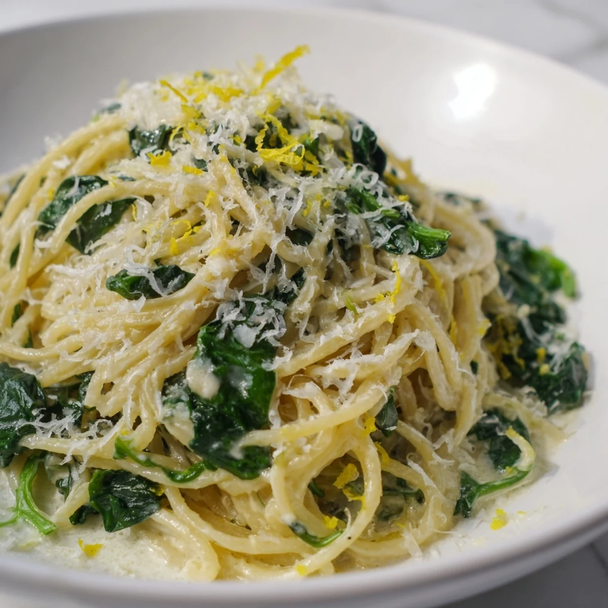 Plate of Creamy Lemon Spinach Spaghetti, glistening with lemon zest and fresh spinach, garnished with grated Parmesan.  
