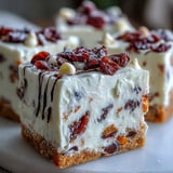 A close-up of frosted Cranberry Bliss Bars garnished with extra cranberries and zesty orange.