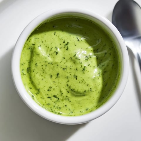 Vibrant green Green Goddess Dressing drizzled over a fresh salad with avocado and cherry tomatoes.  