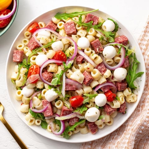 A vibrant bowl of Spring Antipasto Pasta Salad features ditalini tossed with arugula, salami, mozzarella, and pickled vegetables, dressed in a bright lemony vinaigrette.