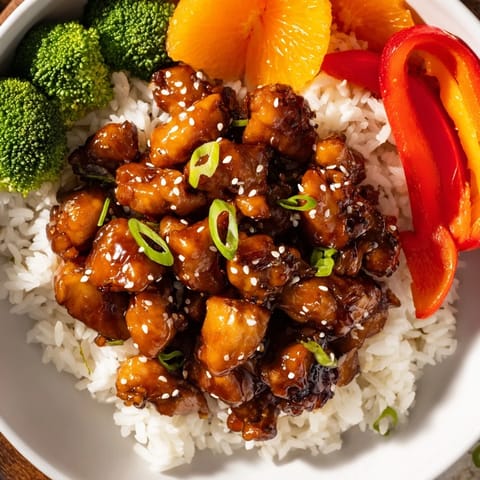 Golden-glazed teriyaki chicken atop fluffy rice with colorful vegetables, a balanced and delicious dinner.