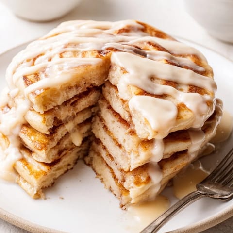A stack of fluffy Cinnamon Roll Pancakes showcases a cinnamon swirl, ready to be devoured at brunch.