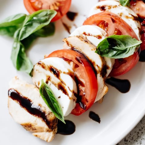 A plated Chicken Caprese Salad showcases juicy grilled chicken layered over mixed greens, cherry tomatoes, and creamy mozzarella with fresh basil. 