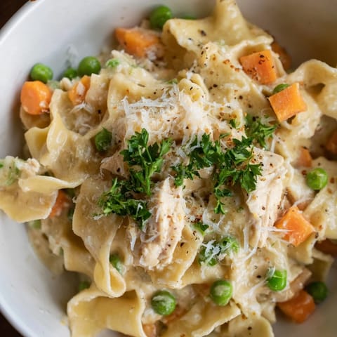 A rustic skillet holds steaming Spring Chicken Noodle Skillet, garnished with fresh parsley and Parmesan, next to a linen napkin and serving spoon.  