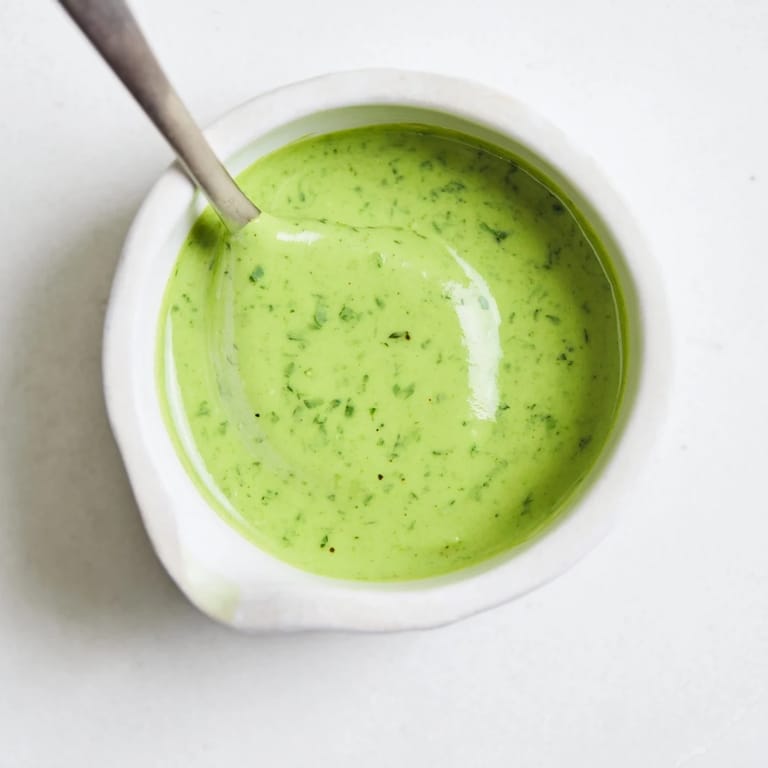 Bright Green Goddess Dressing in a glass jar beside crisp vegetables and toasted bread.